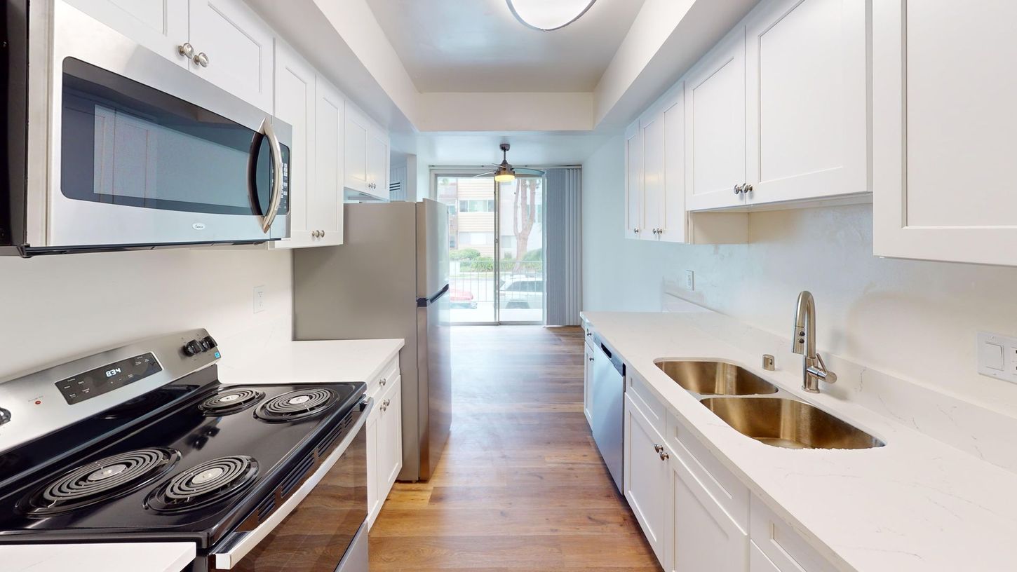 Bright white kitchen with stainless steel appliances, white countertops, and wood floor. View opens to a patio.