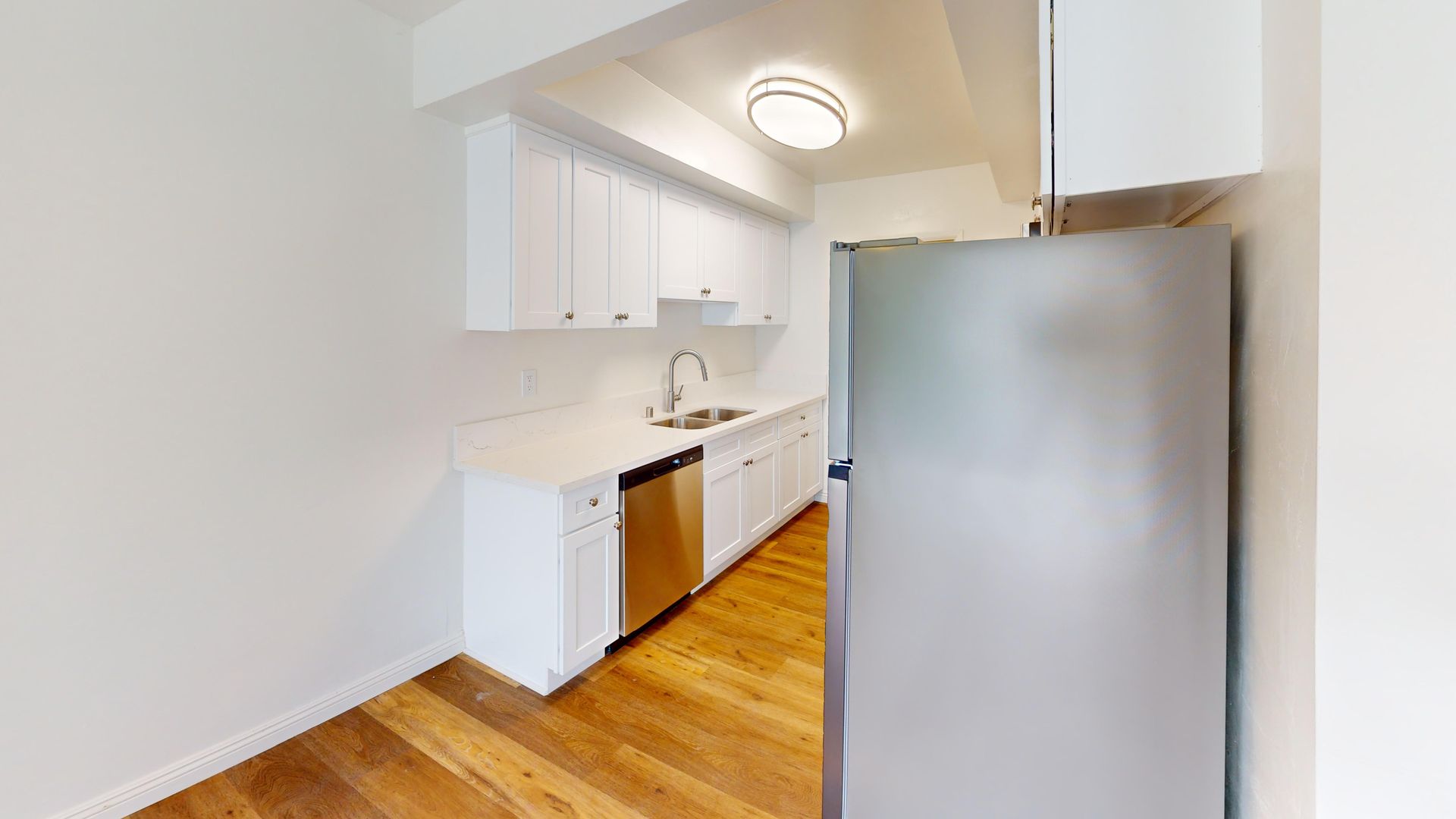 White kitchen with stainless steel appliances, white cabinets, light countertop, and wood floor.