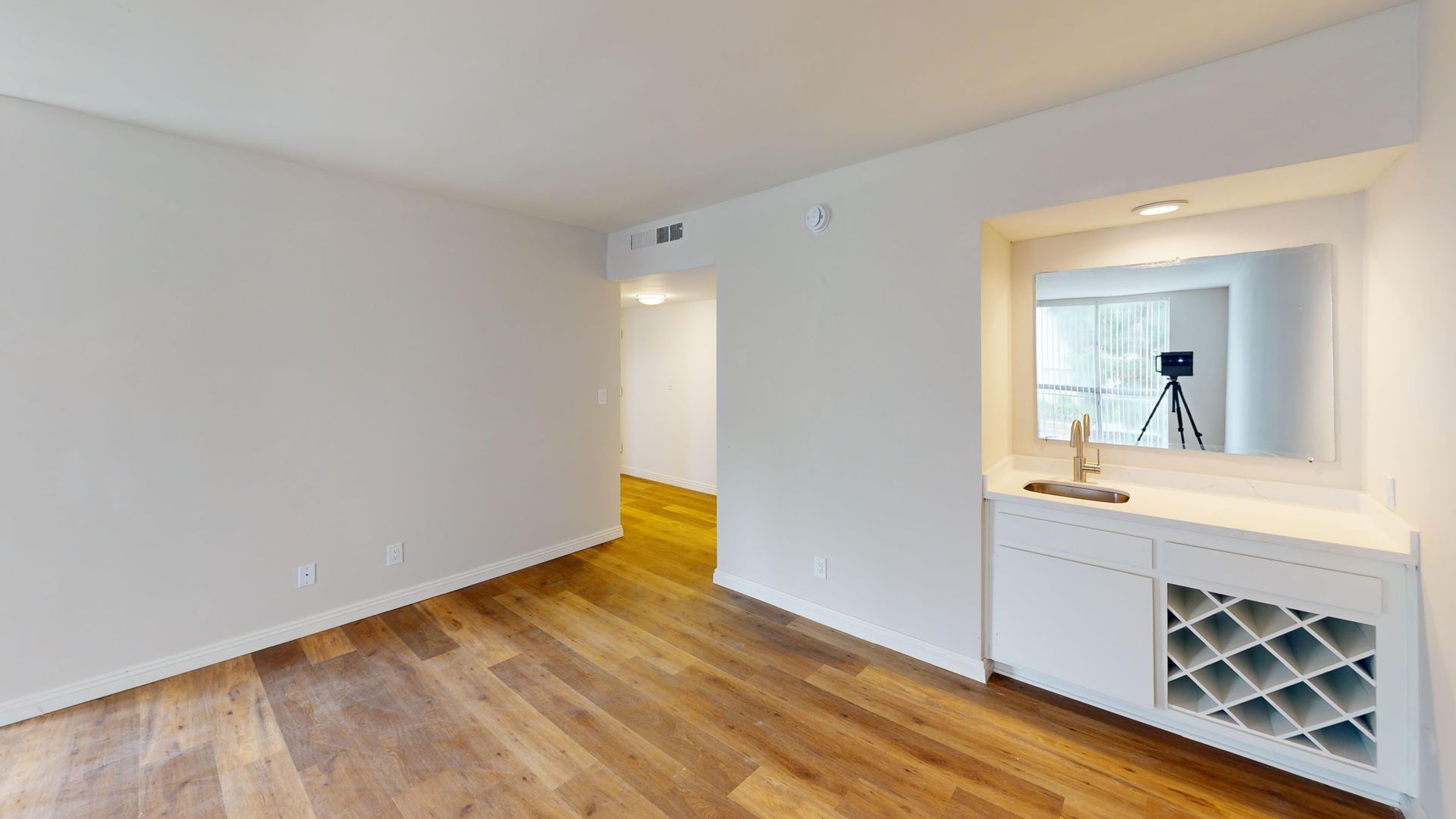 Empty room with hardwood floors, white walls, and a built-in bar area with sink and wine rack.