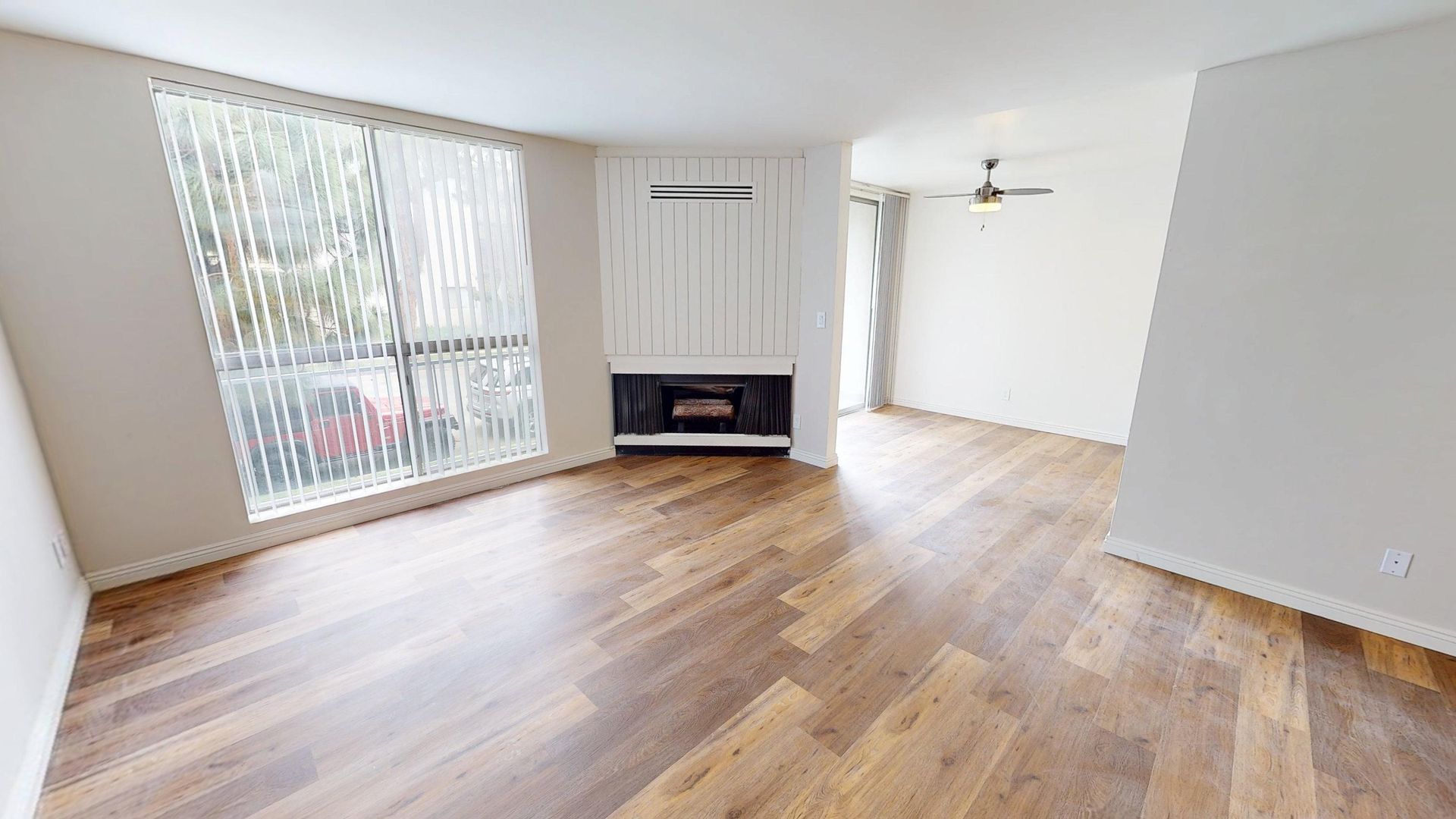 Empty living room with wood flooring, fireplace, and large window.