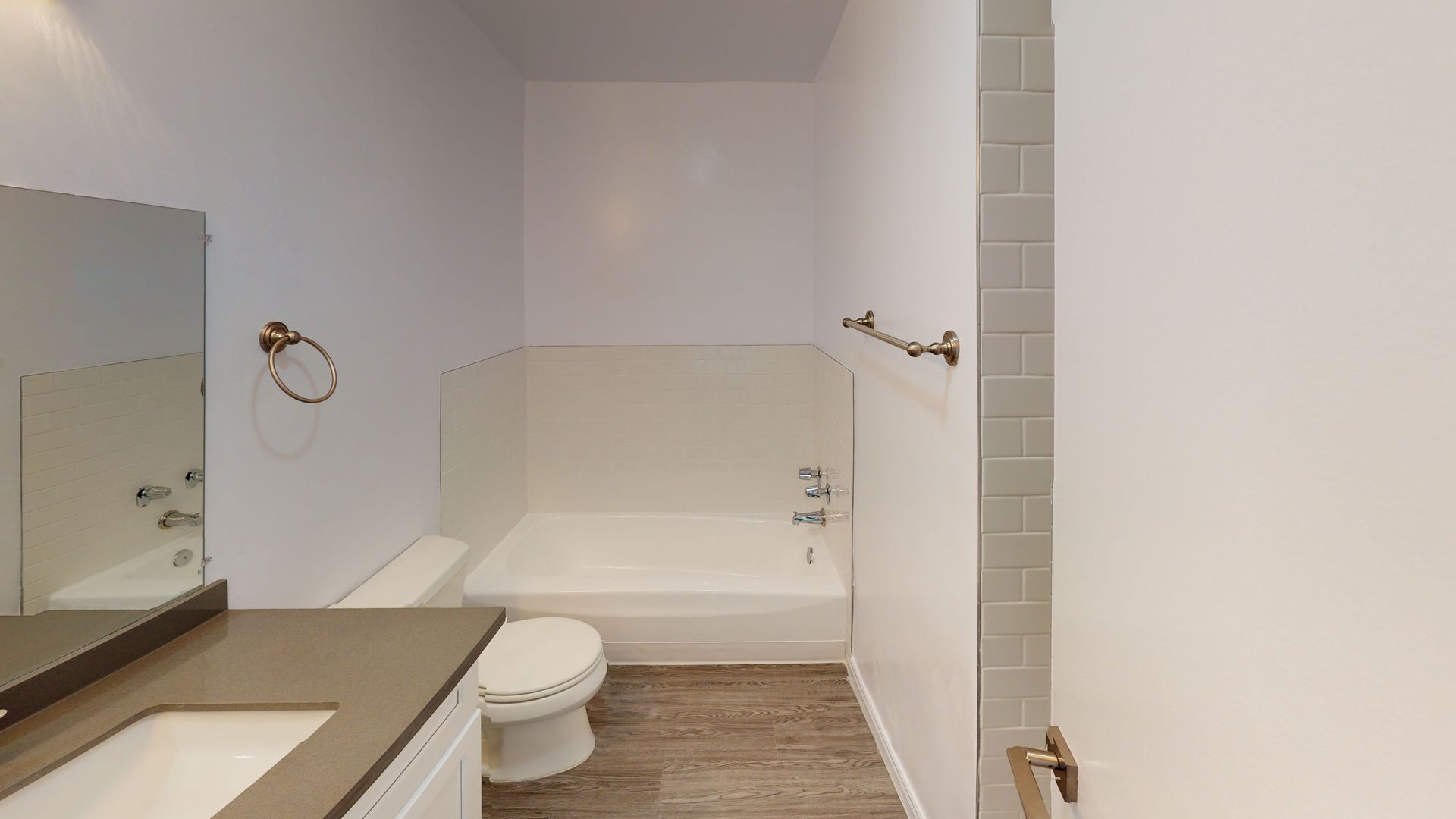 Bathroom with a toilet, vanity, and bathtub. White walls, grey floor, and stainless steel fixtures.