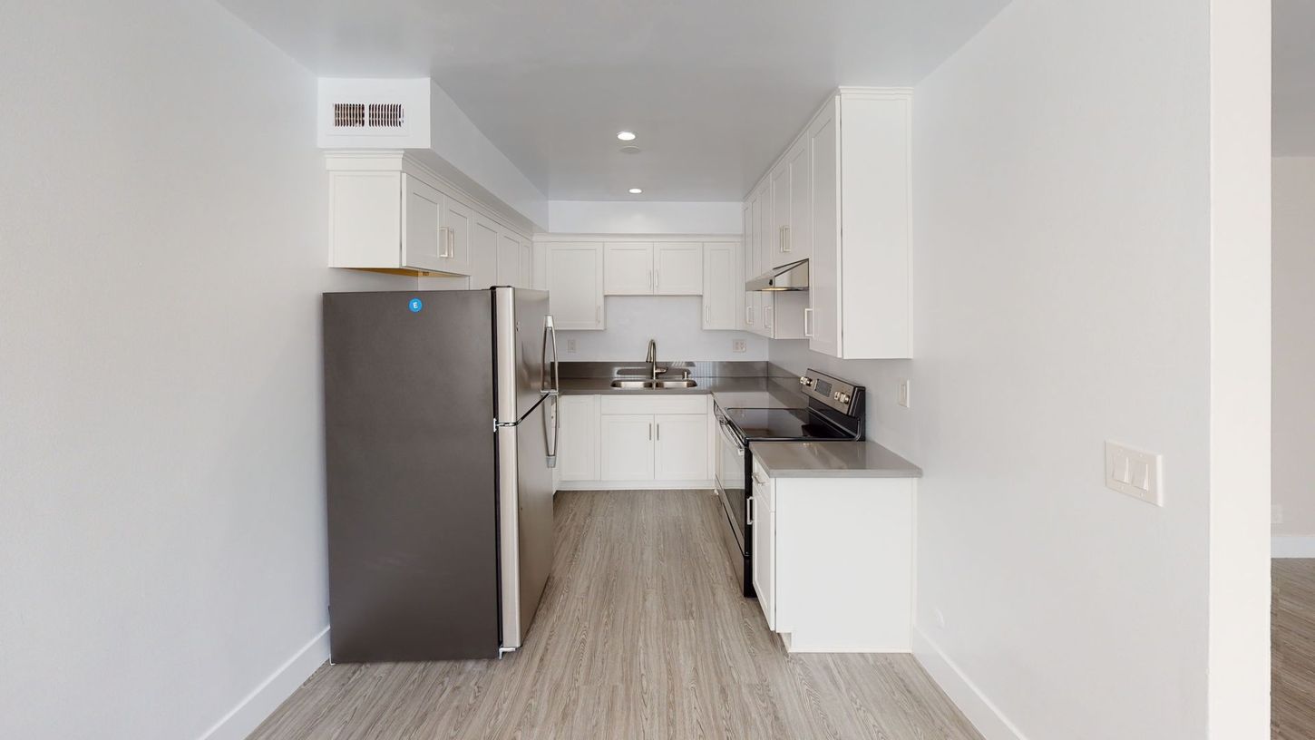 Kitchen with white cabinets, dark refrigerator, and gray flooring.