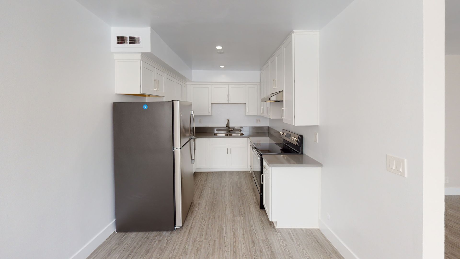 Kitchen with white cabinets, dark refrigerator, and gray flooring.