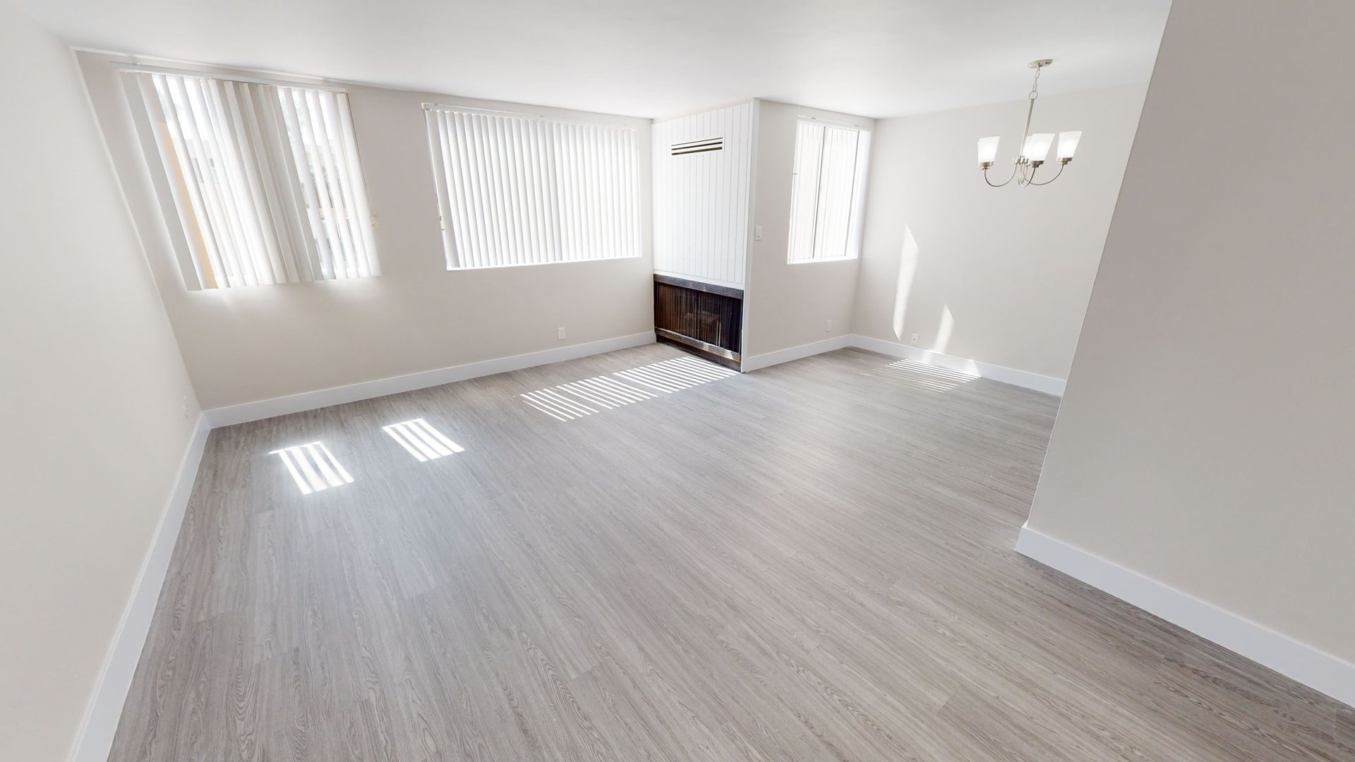 Empty, bright room with gray flooring, white walls, and curtains. Sunlight streams through the windows.