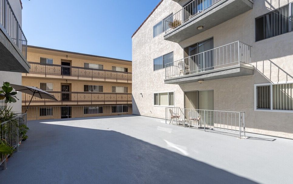Exterior view of beige apartment buildings, gray patio, clear blue sky.