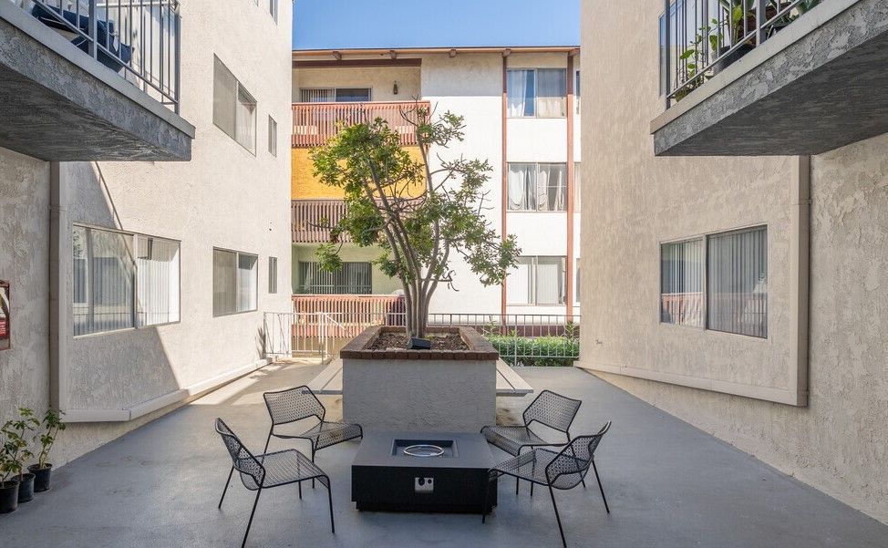 Courtyard with seating around a fire pit, between two apartment buildings, with a tree in the center.