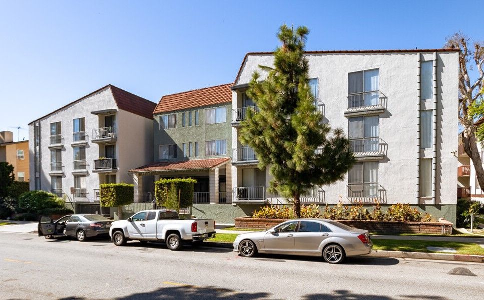 Apartment building with stucco exterior; cars parked on street in front.