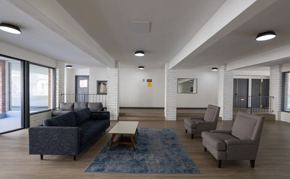 Lobby with a blue sofa, two armchairs, coffee table, and area rug. White pillars and ceiling.