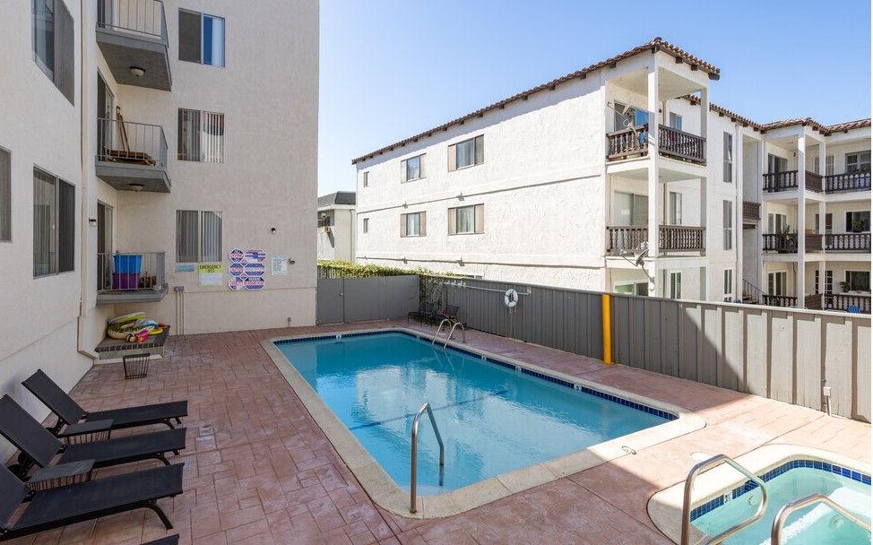 Pool area with a rectangular pool, lounge chairs, and apartment buildings.