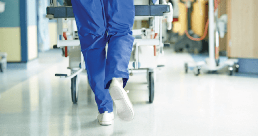 A nurse is pushing a hospital bed down a hospital hallway.