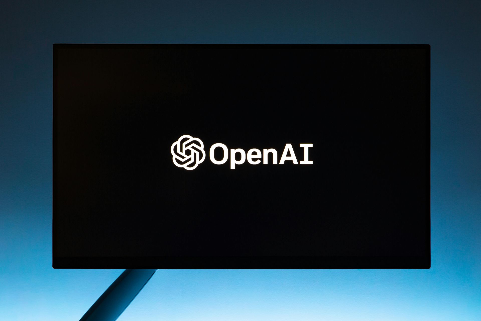 OpenAI logo on a black screen, with a blue gradient background.