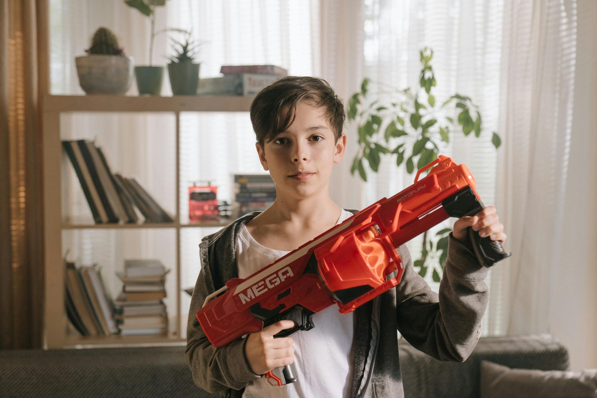 Boy holding a large red toy gun indoors, looking at the camera.