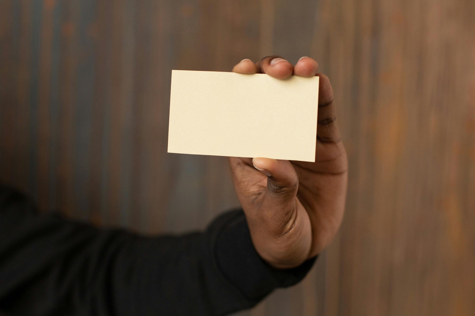 Hand holding a blank, cream-colored rectangular card against a mottled brown background.