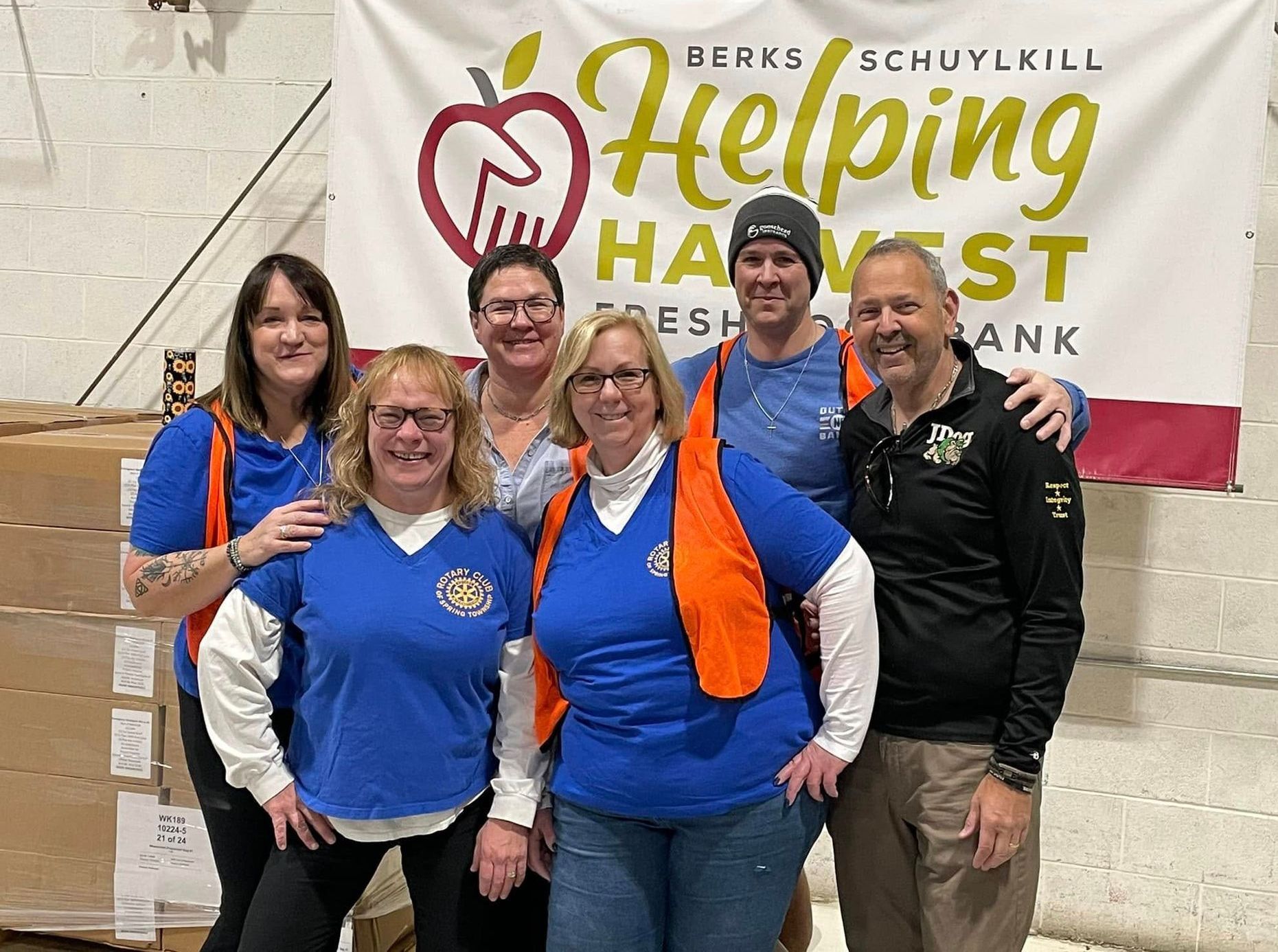 A group of people are posing for a picture in front of a helping harvest banner.