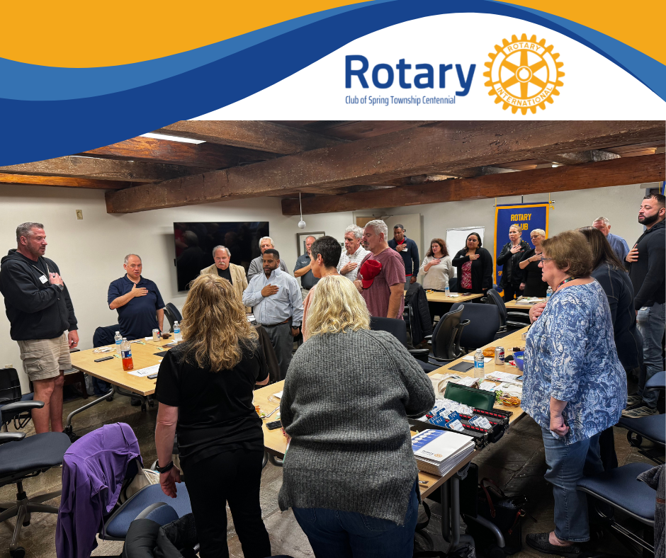 A group of people are standing around a table with a rotary logo in the background.