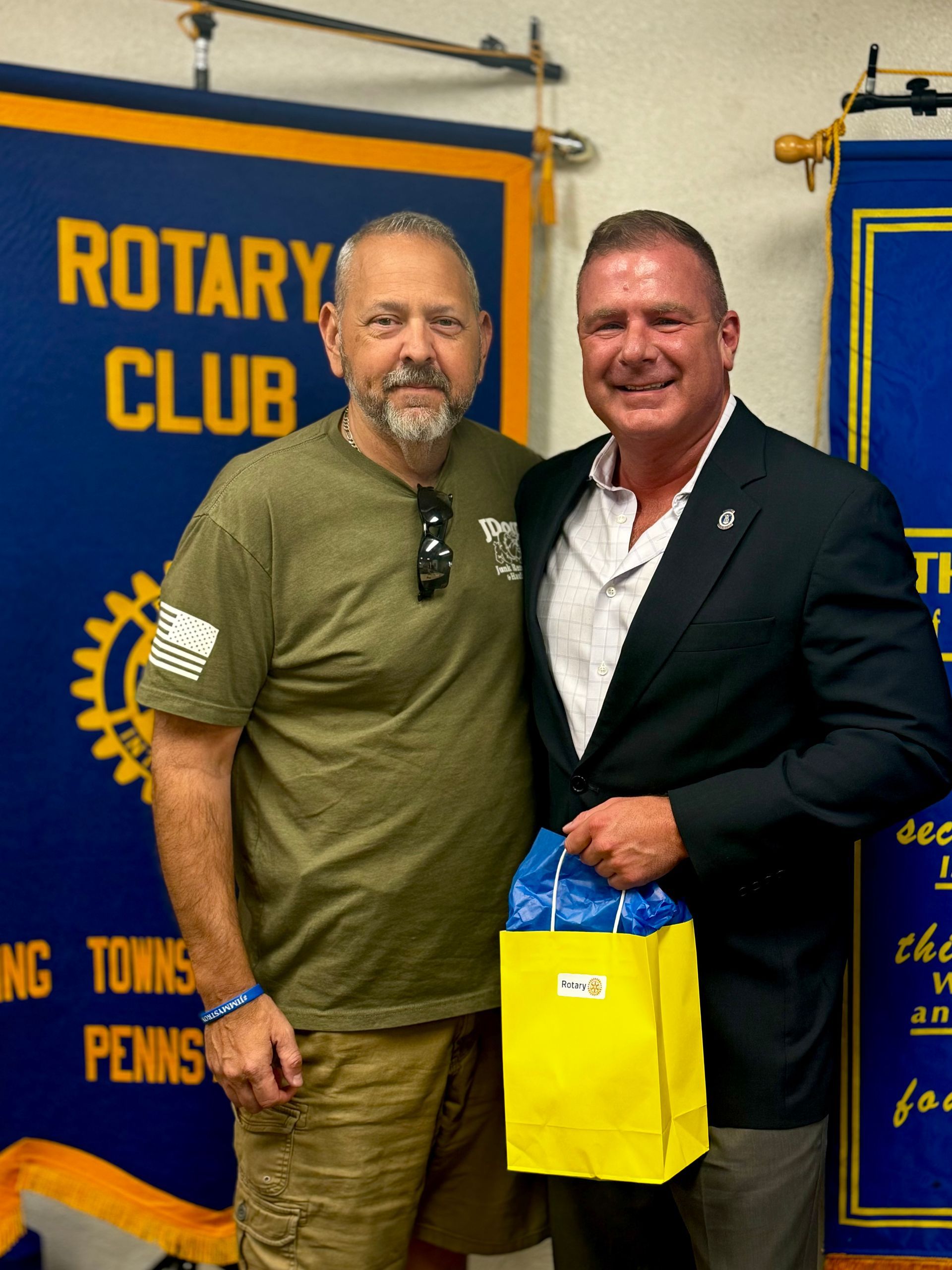 Two men are posing for a picture in front of a banner that says rotary club
