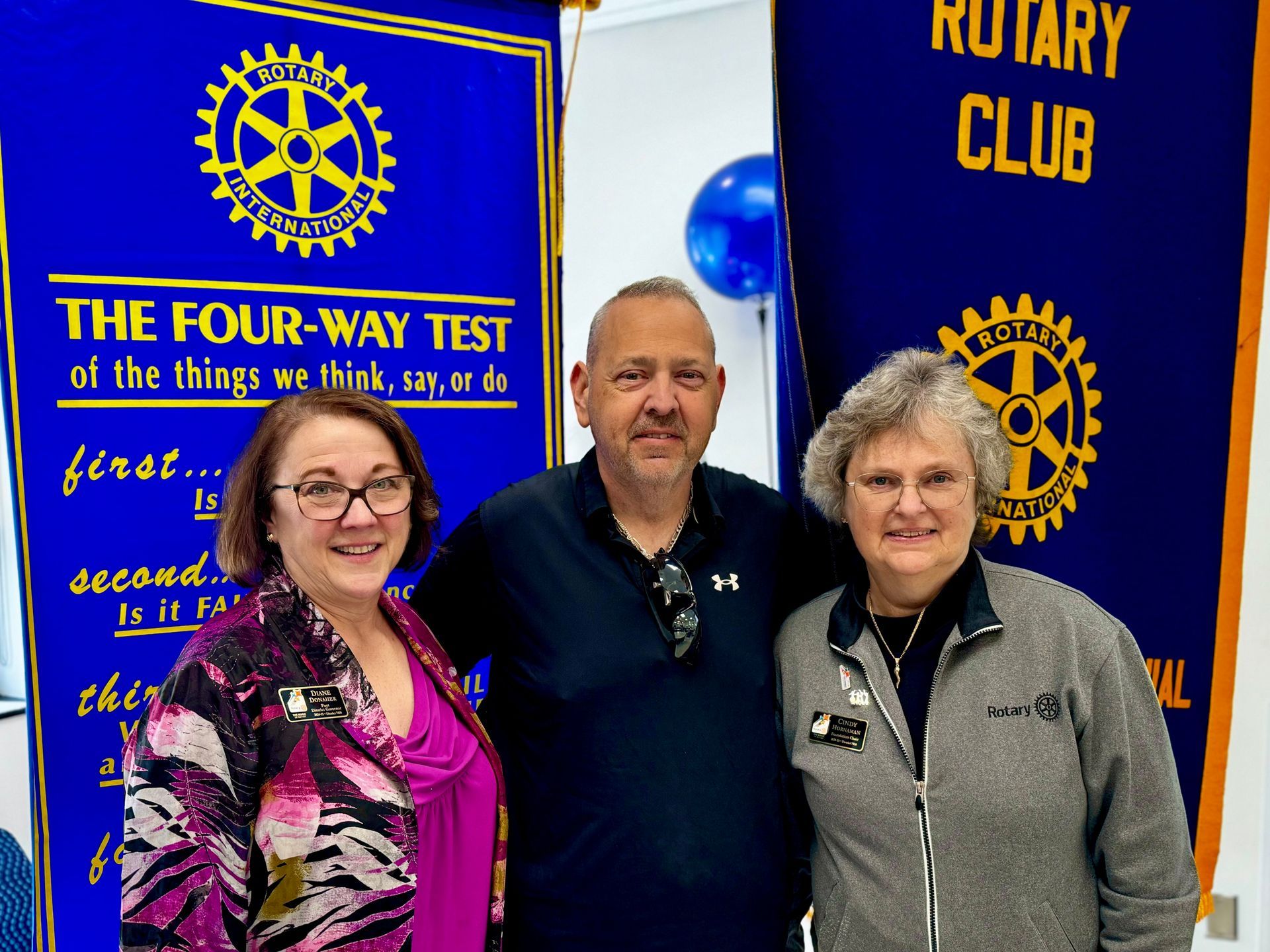 Three people are posing for a picture in front of a rotary club banner
