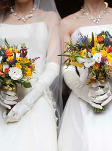 Two brides wearing their wedding dress and holding their bouquet