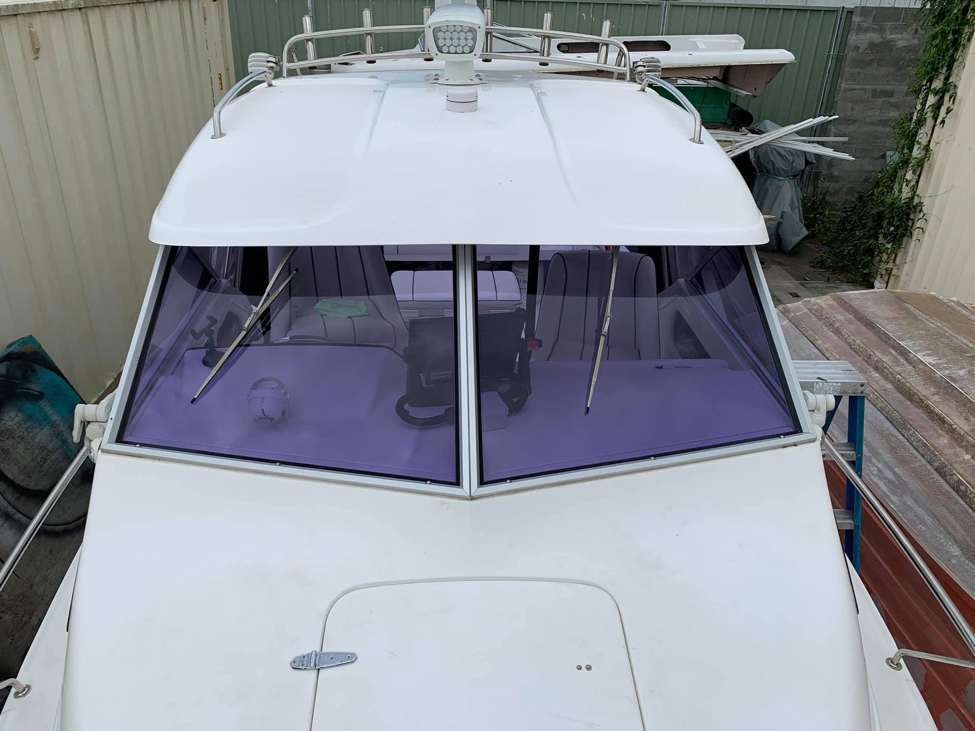 A white boat with a purple windshield is parked in a yard.