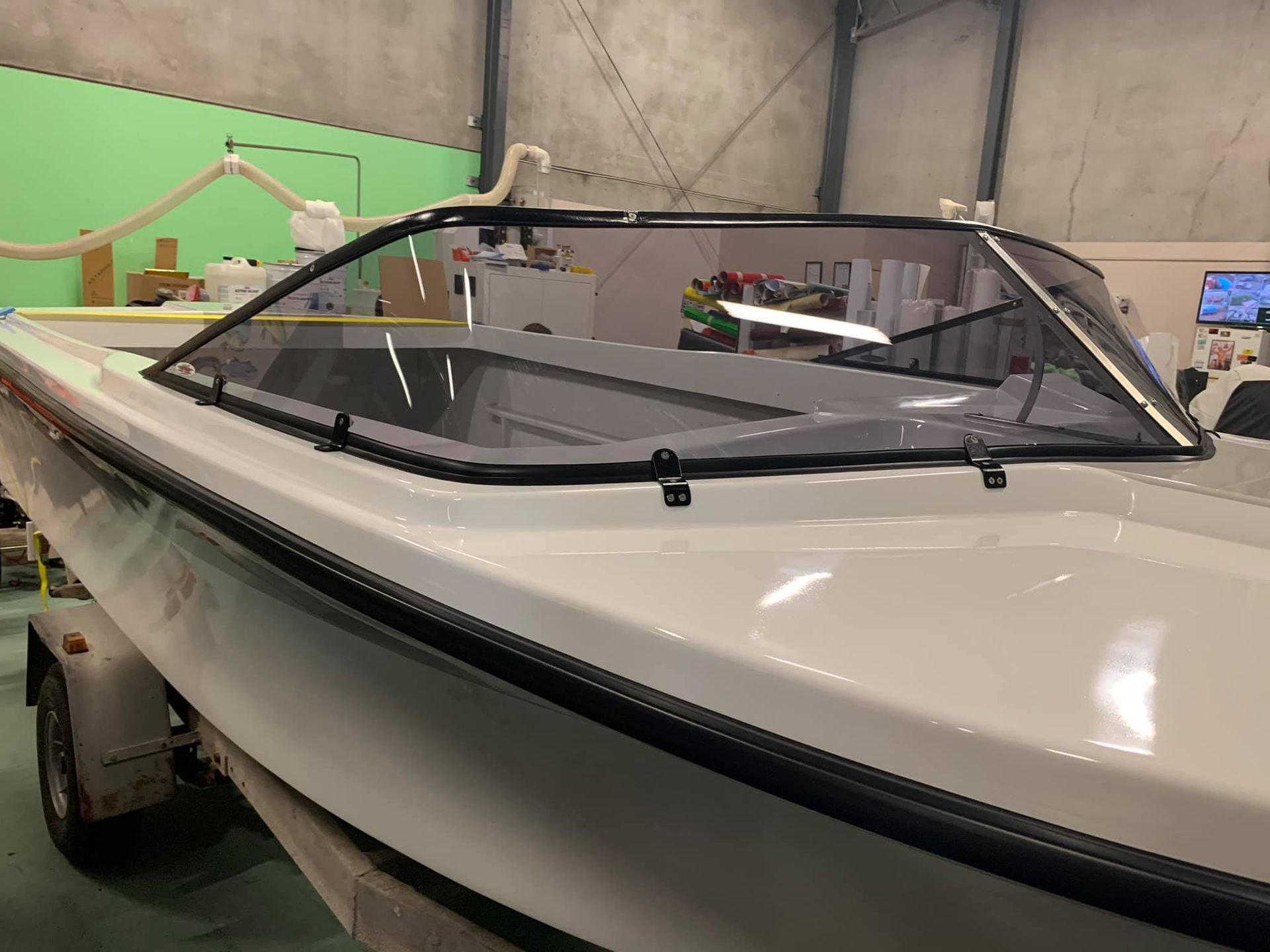 A white boat with a windshield is sitting in a warehouse.