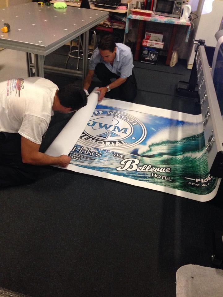 Two men are working on a large poster on the floor - Plastiglass Mid North Coast, NSW