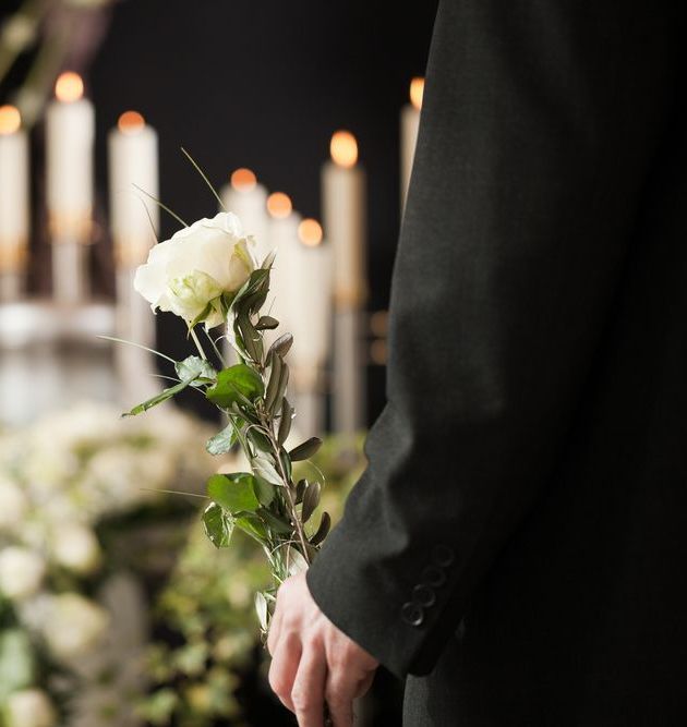 A Man In A Suit Is Holding A White Rose In Front Of Candles — United Funeral Care In Kempsey, NSW