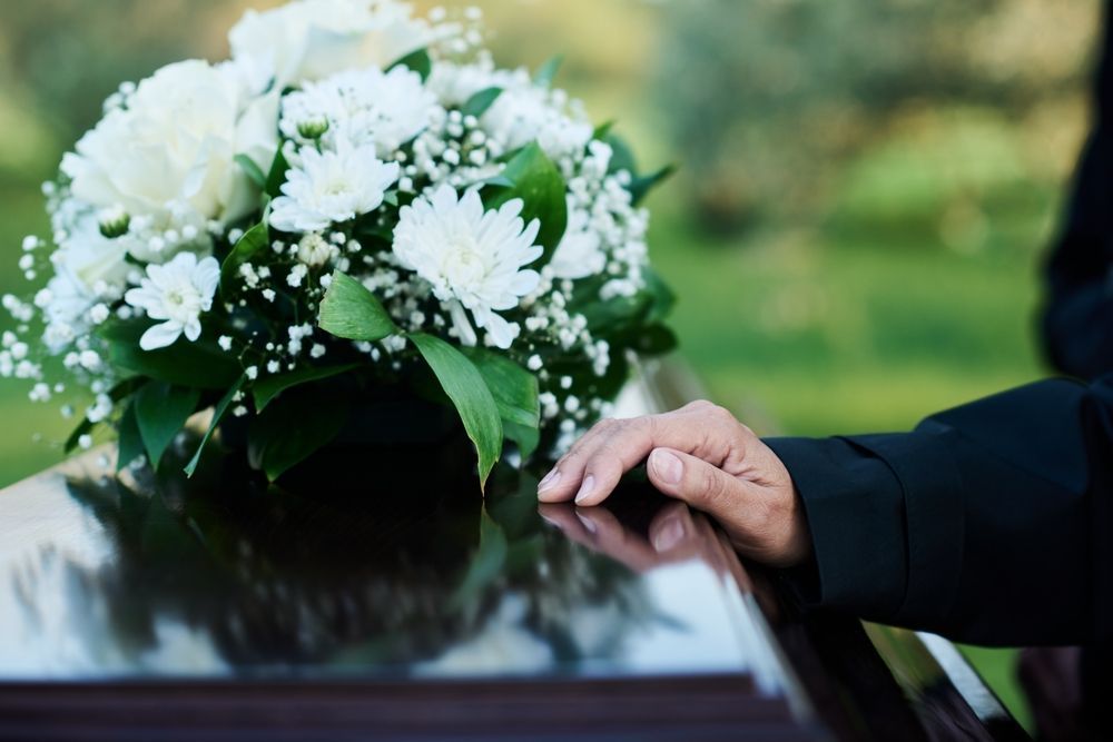A Person Is Standing Next To A Coffin With Flowers On It — United Funeral Care In Kempsey, NSW