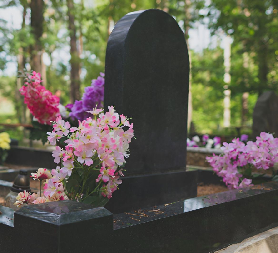 A Black Gravestone Surrounded By Pink And Purple Flowers — United Funeral Care In Kempsey, NSW