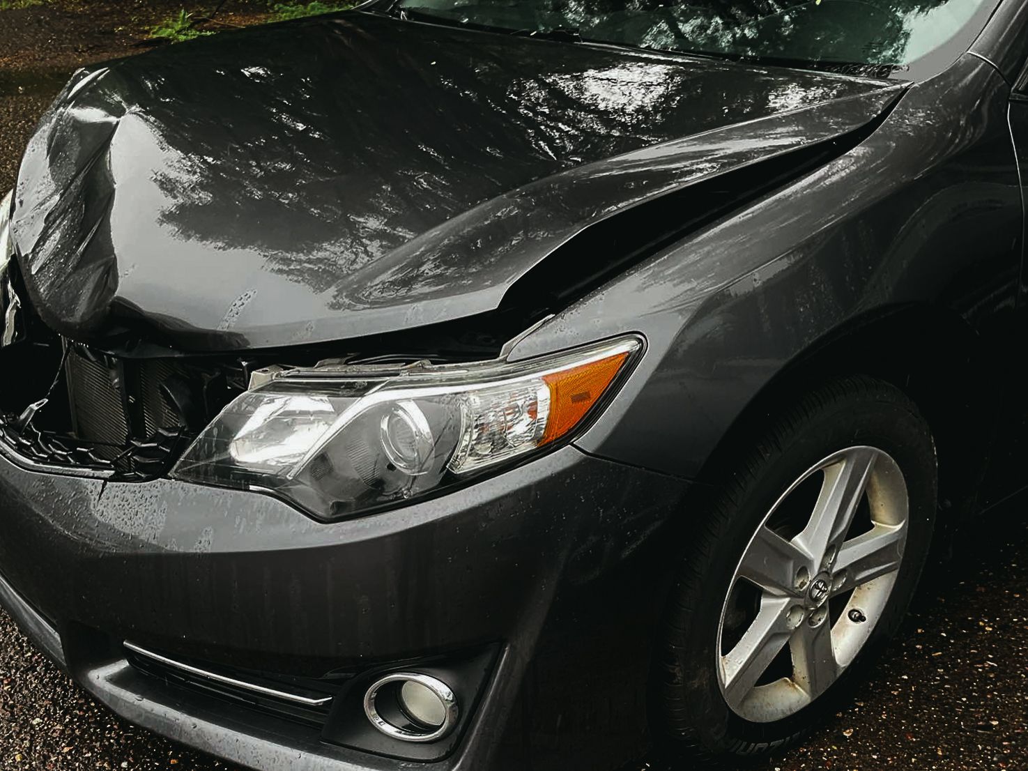 A gray car with a damaged hood is parked on the side of the road.