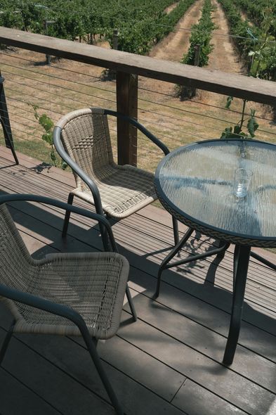 Patio table and chairs on a wooden deck overlooking a vineyard with rows of grapevines.
