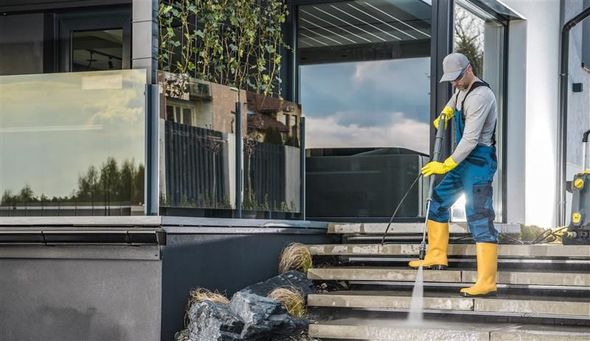 Person in yellow boots and gloves pressure washes outdoor steps.