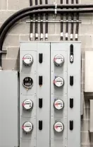 Gray electrical breaker panels and conduit mounted on a cinderblock wall in an industrial room
