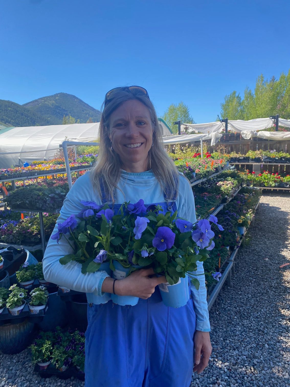 A woman is holding a bouquet of purple flowers in a greenhouse.