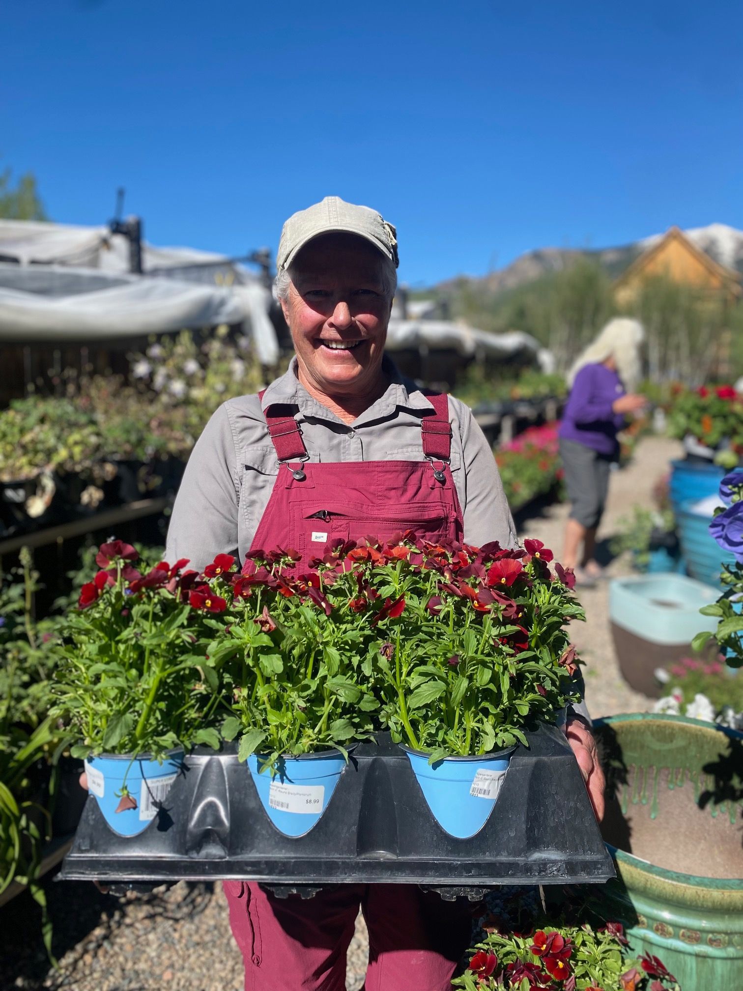 A woman is holding a tray of flowers in a garden center.