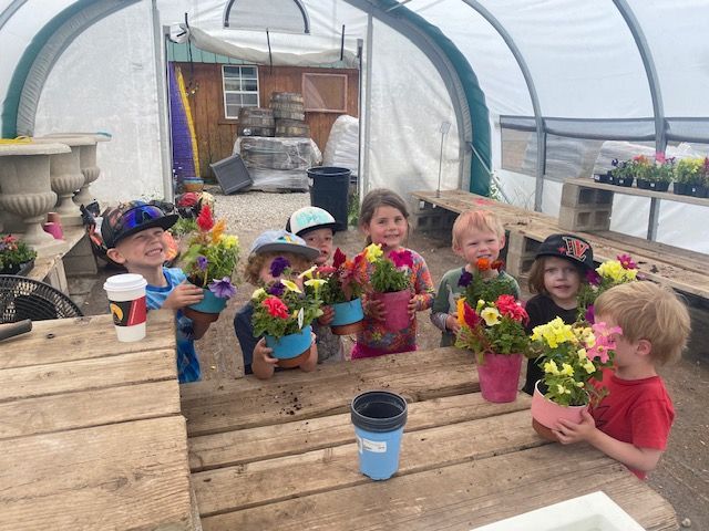 Children in a greenhouse holding colorful potted flower arrangements they have made.