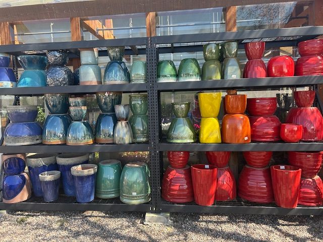 Two metal shelves filled with various ceramic pots in shades of blue, green, yellow, orange, and red.