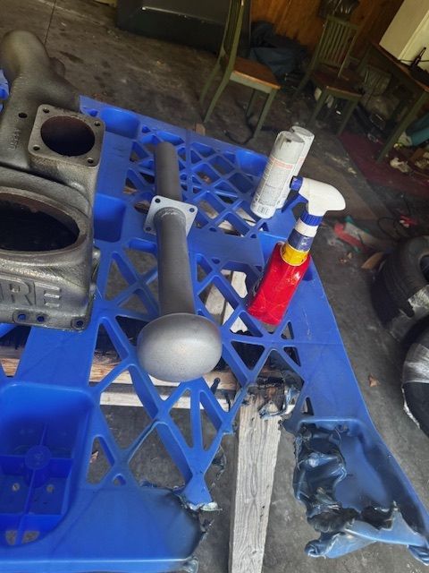 Gray car parts and spray bottles on a blue pallet in a garage.
