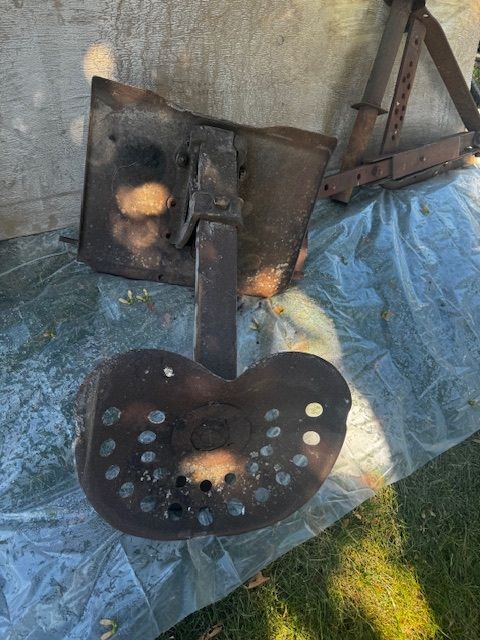 Rusty tractor seat with a support bracket, outdoors on a tarp.