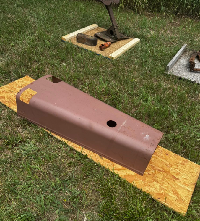 A piece of metal is laying on a piece of wood in the grass.