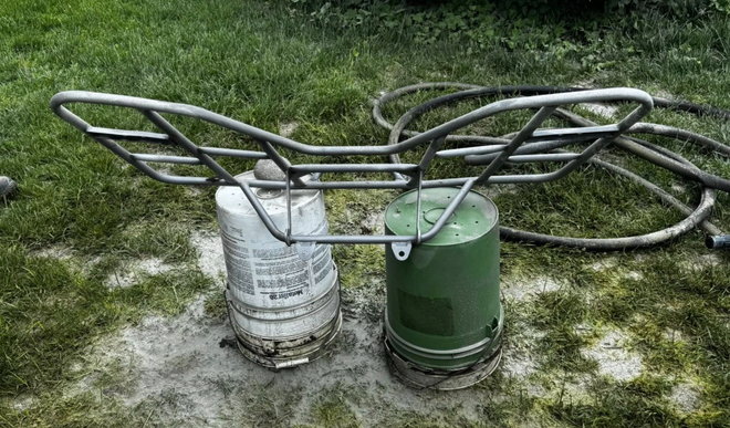 A metal frame is sitting on top of a green bucket in the grass.