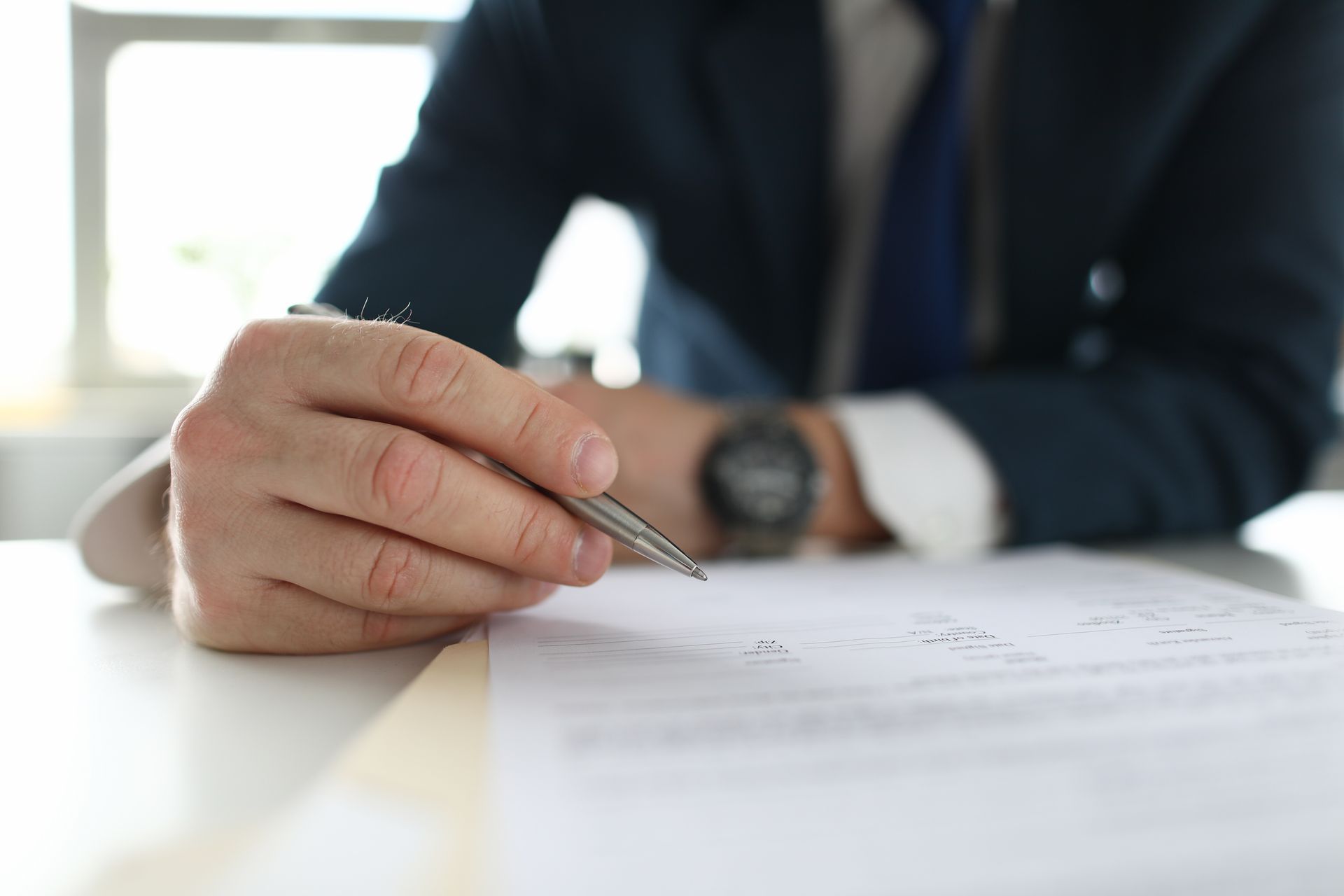 A man is sitting at a table holding a pen and writing on a piece of paper.
