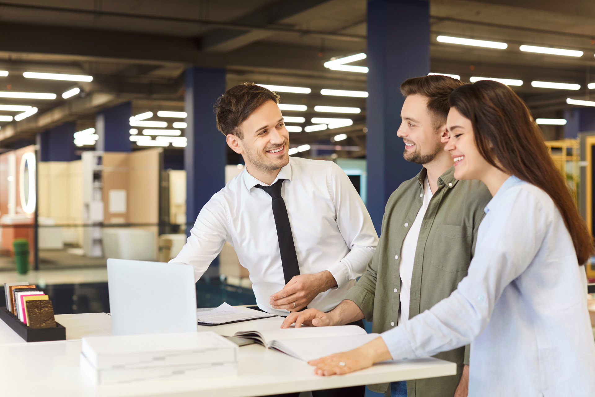 A man is talking to a woman and a man while a woman looks at a laptop.