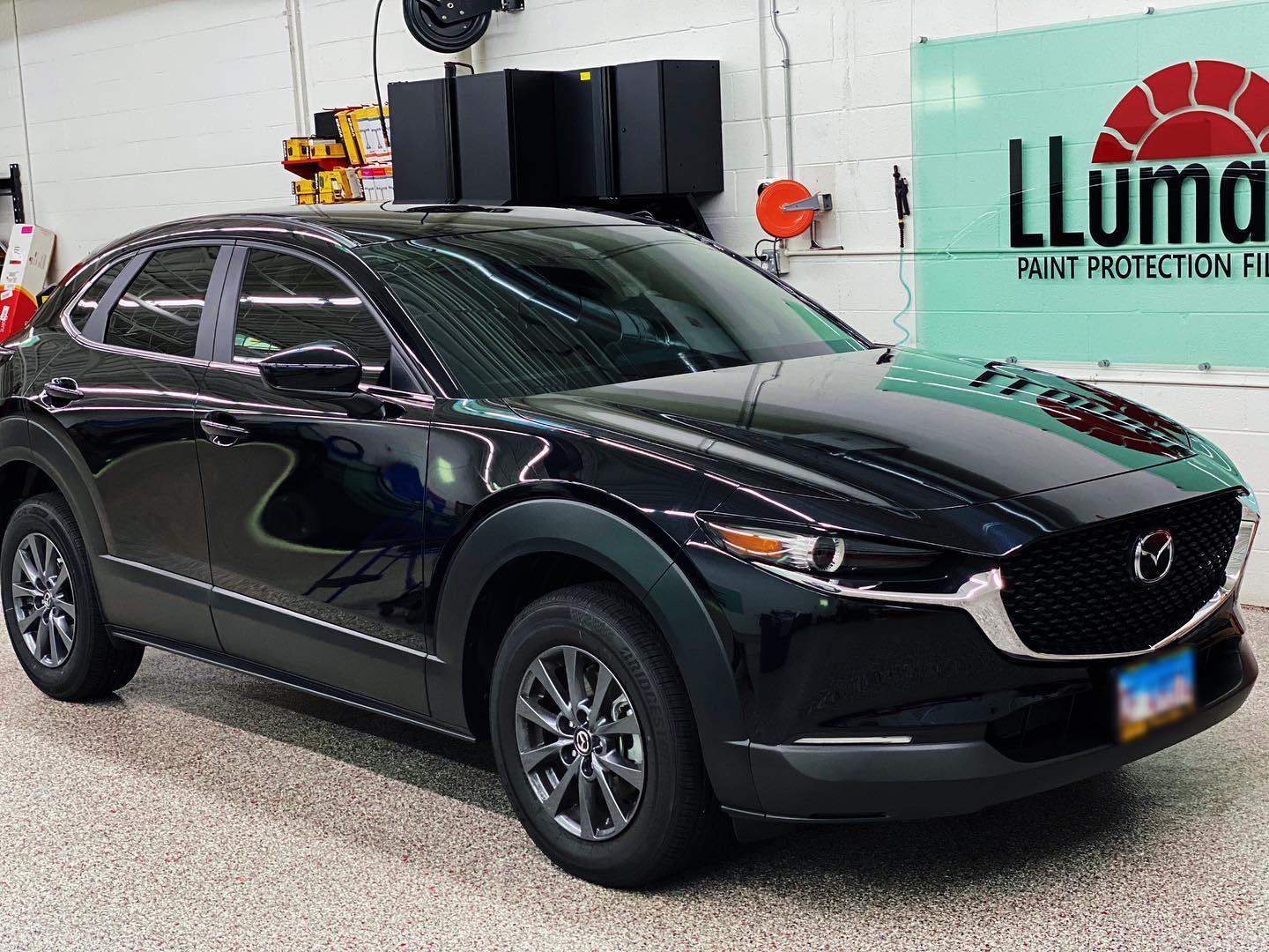 A black mazda cx-30 is parked in a garage next to a sign that says lluma.