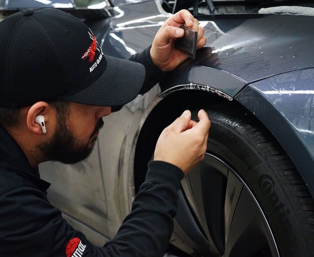 A man is applying a protective film to the fender of a car.