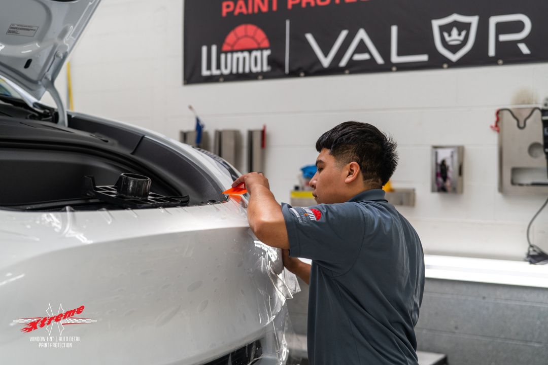 A man is wrapping a car in paint protection film in a garage.