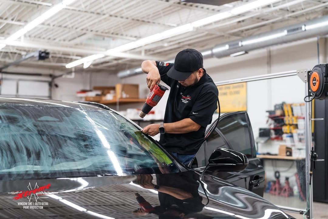A man is working on tinting a car windshield in a garage.