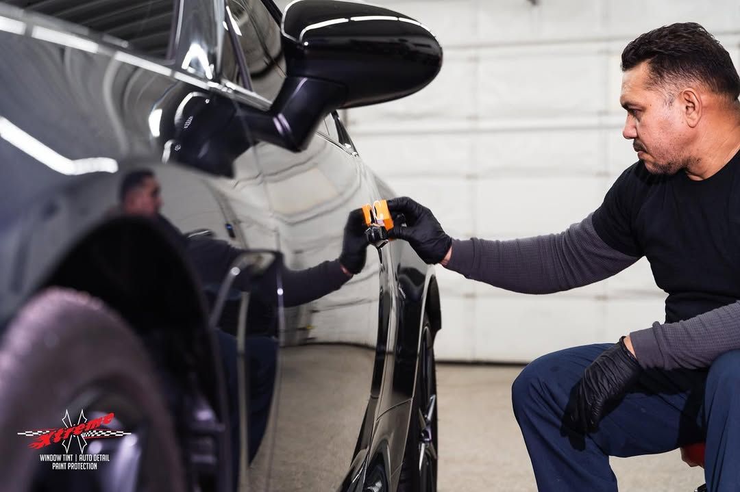 A man is kneeling down in front of a black car.