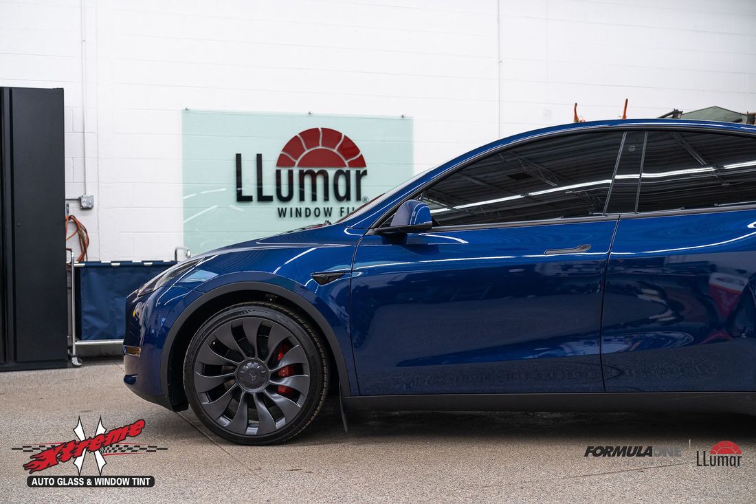 A blue tesla model y is parked in front of a sign that says llumar.
