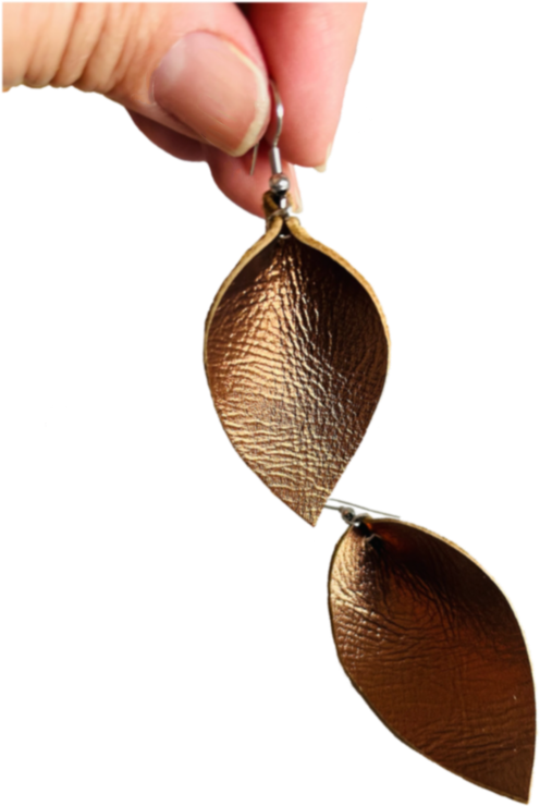 Una persona sostiene un par de pendientes de cuero con forma de hoja de oro.