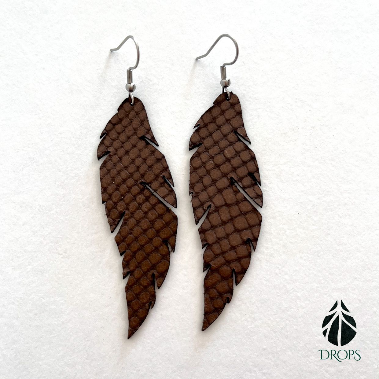 Un par de pendientes marrones con forma de pluma hechos de piel de serpiente.